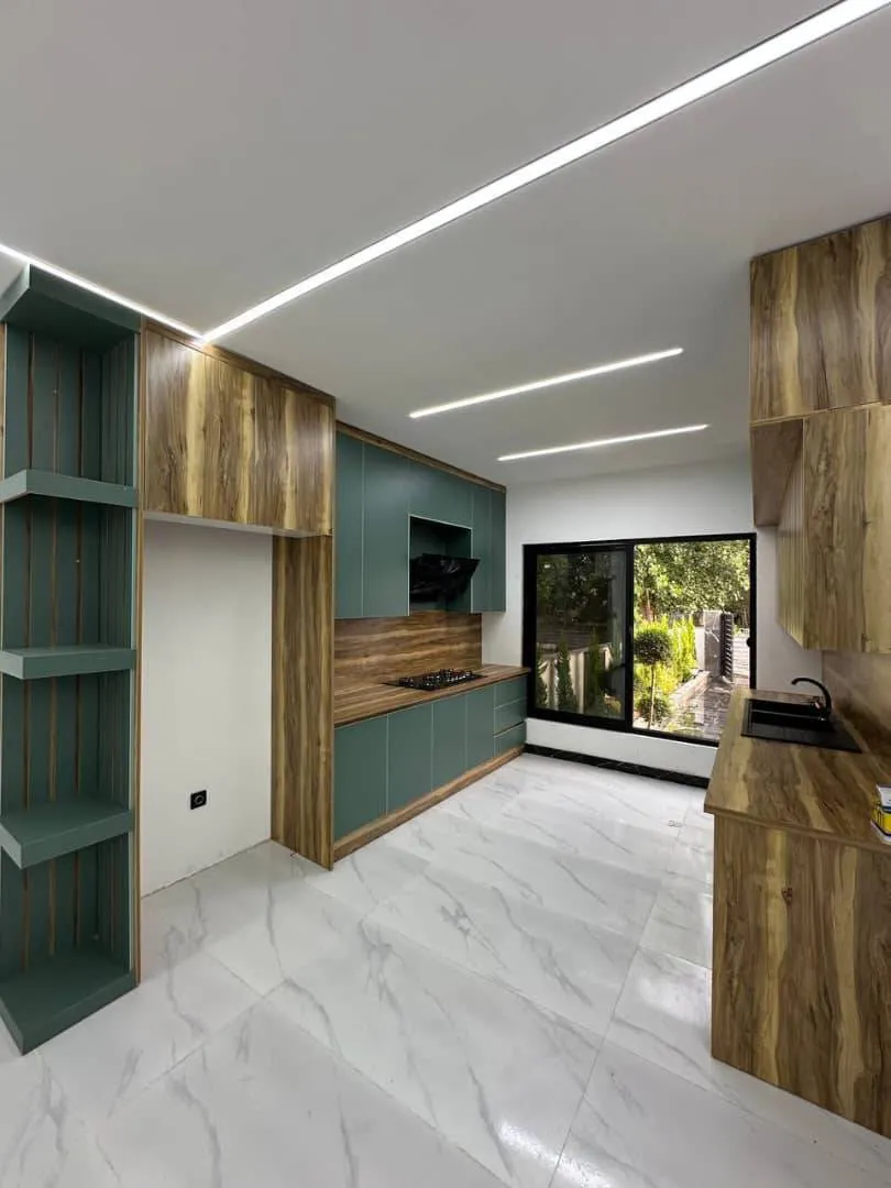 آشپزخانه مدرن با کابینت سبز-چوبی و نورپردازی خطی در ویلای چمستان